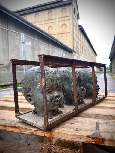 Three bronze baby head molds with serene features, one with silicone insert, in original aged steel frame outdoors.
