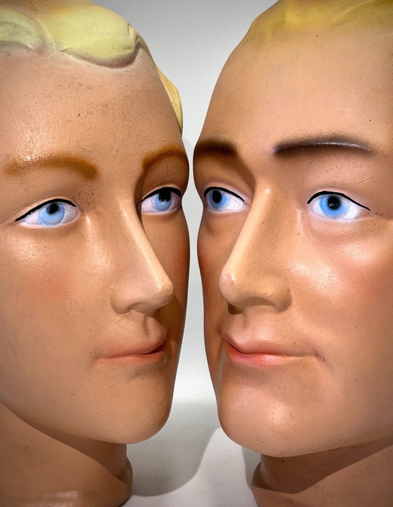 Pair of vintage ceramic mannequin heads with stylized features and retro hair, mounted on black stands, c. 1950s–60s