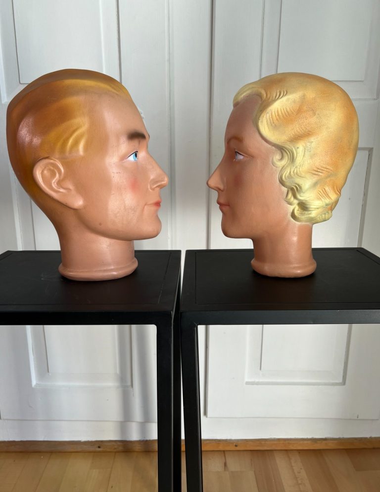 Pair of vintage ceramic mannequin heads with stylized features and retro hair, mounted on black stands, c. 1950s–60s